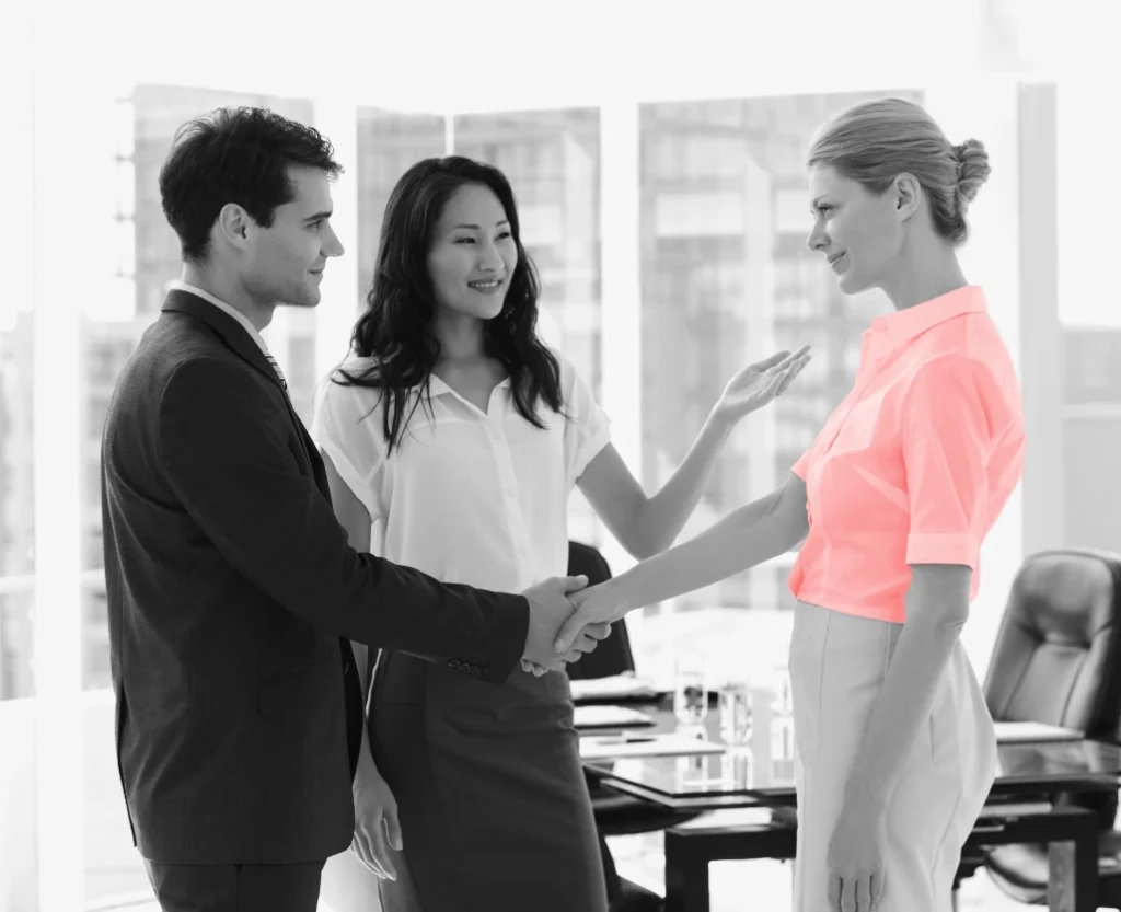 Business professionals shaking hands in a modern office, woman wearing red shirt as accent
