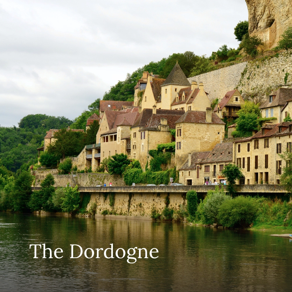 Historic village in the Dordogne set along the river beneath limestone cliffs and lush greenery.