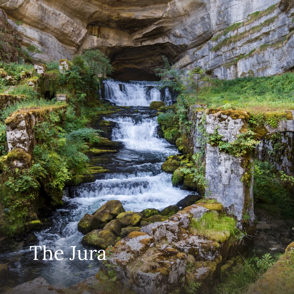 Source of the Loue waterfall cascading through a rocky gorge surrounded by lush greenery in the Jura Mountains, France